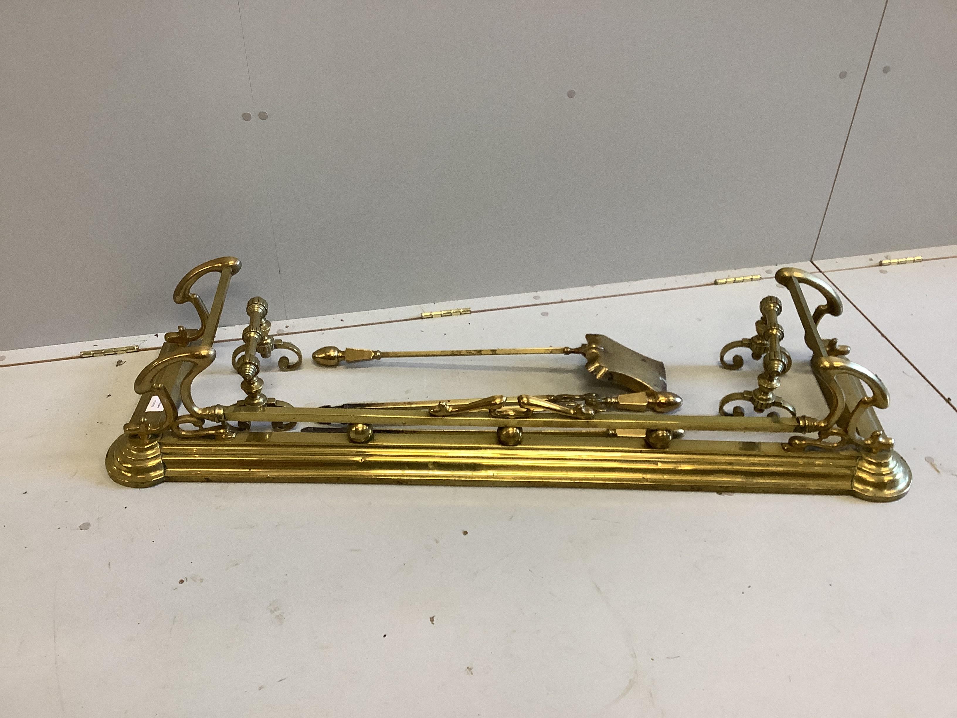 A Victorian Art Nouveau brass fender, length 136cm together with a set of three implements and a pair of firedogs